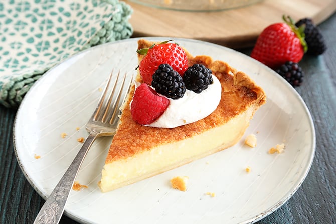 Slice of Buttermilk Pie on white plate with whipped topping and fruit on top