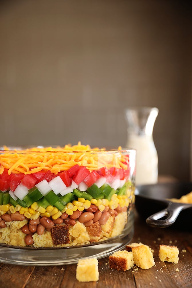 Layered Cornbread Salad in clear glass bowl - ranch dressing in the background