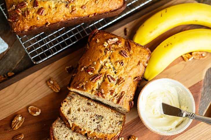 Sliced Banana bread with bananas on cutting board.