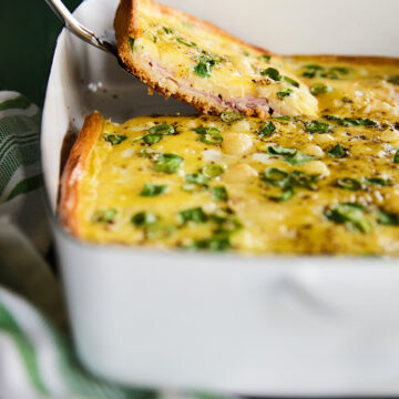 Slice of Ham and swiss breakfast casserole in a white dish.