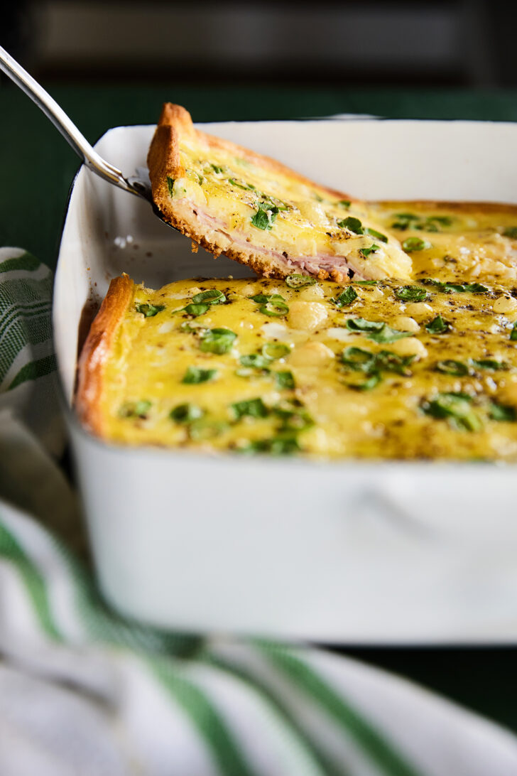 Slice of Ham and swiss breakfast casserole in a white dish.