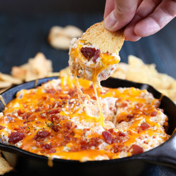 Cheesy Chicken Bacon Ranch Dip scooping out of  pan with a chip