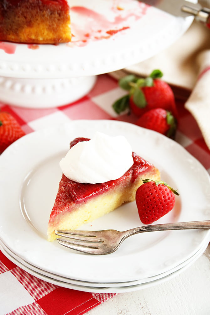 Slice of Strawberry Upside Down Cake on white dish with whipped topping and strawberry served on side