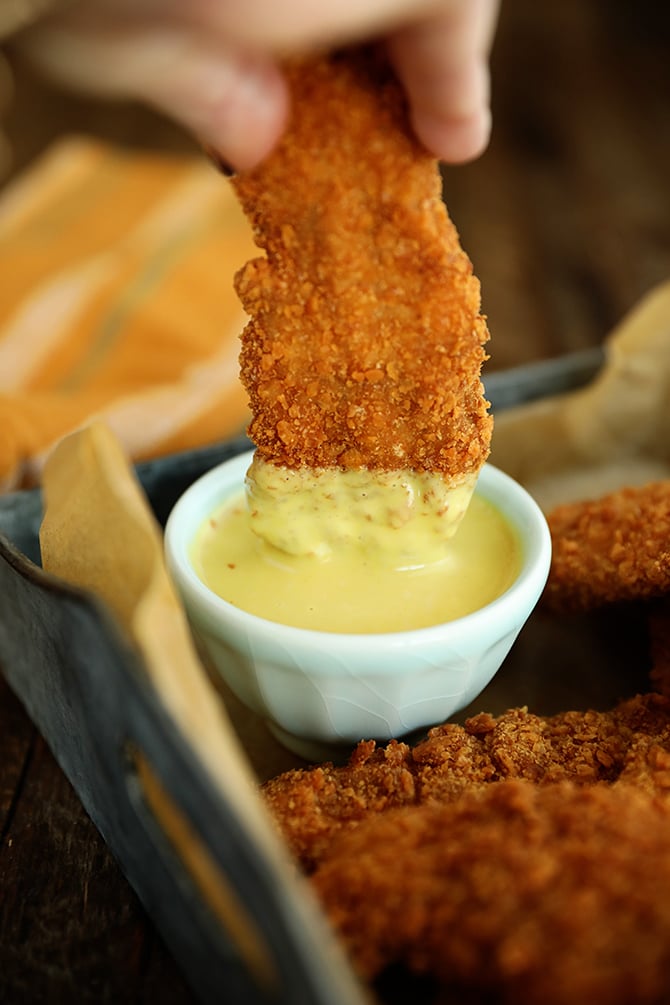 Saltine Crusted Chicken Tender being dipped in honey mustard
