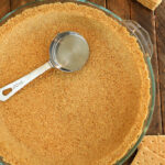 Overhead view of graham cracker crust with measuring cup.