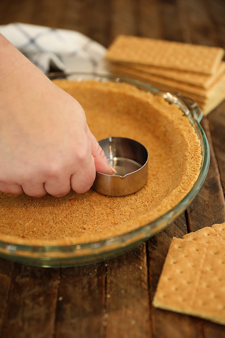 Hand pressing graham cracker crust into plate.