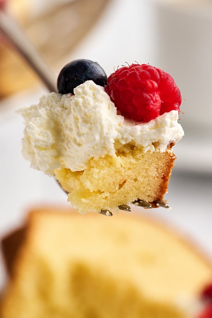 Bite of Cream Cheese Pound Cake with whipped cream and berries.
