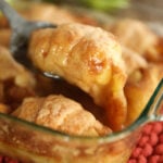 Scooping apple dumpling out of dish.